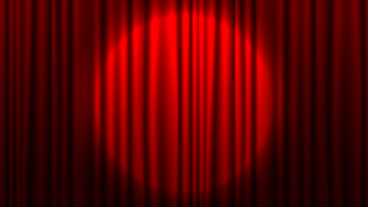 Red theater curtain partially open with spotlight on stage
