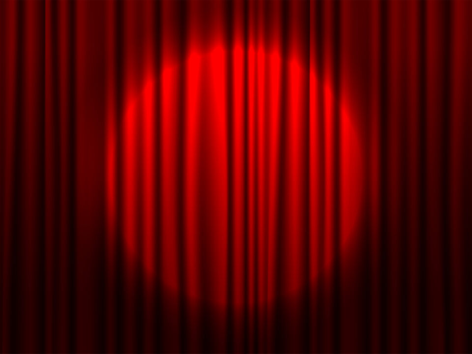 Red theater curtain partially open with spotlight on stage